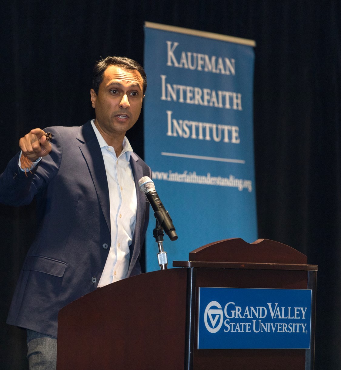 Eboo Patel presenting at GVSU with Kaufman Interfaith Institute banner in background